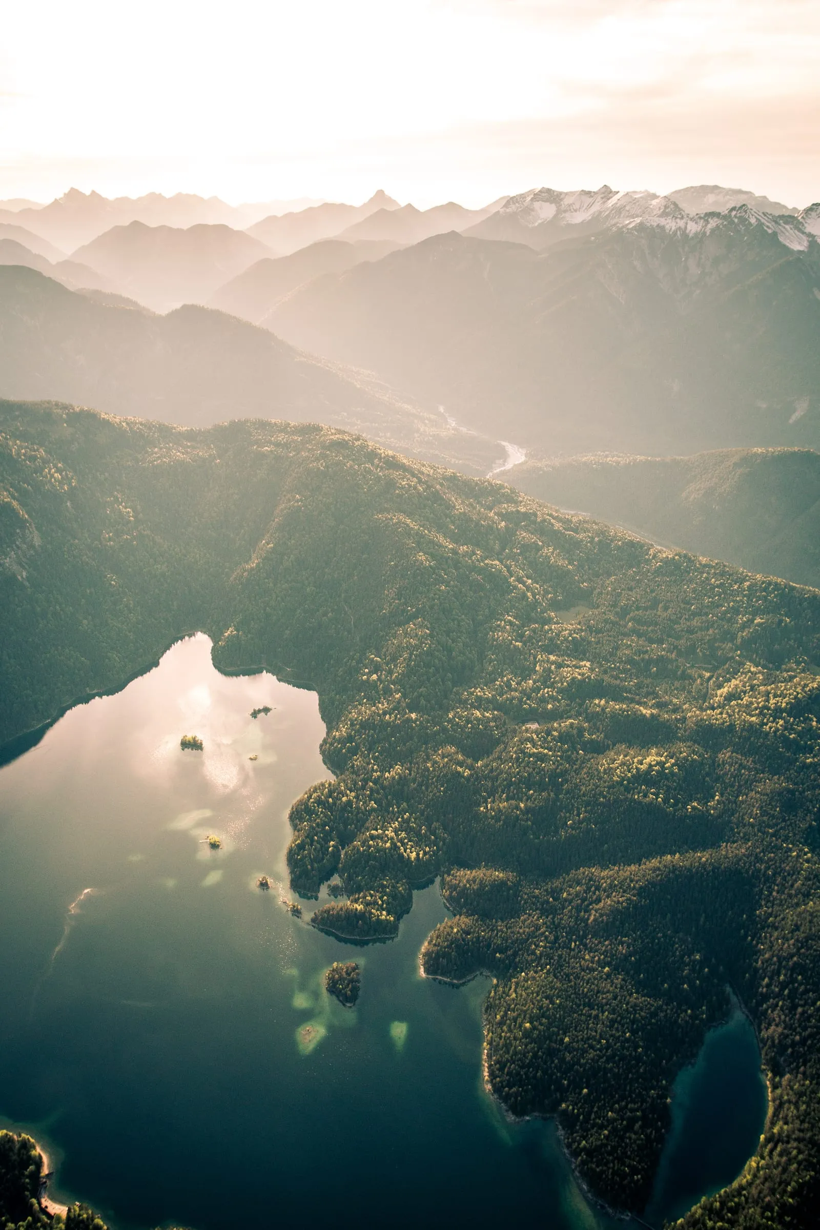 Bergsee zwischen bewaldeten Hängen im warmen Abendlicht, von oben gesehen