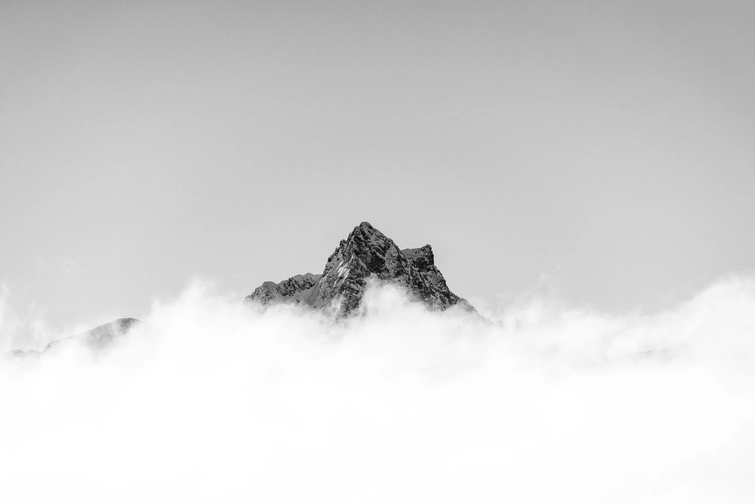 Ein einzelner Berggipfel ragt aus einer weißen Nebeldecke
